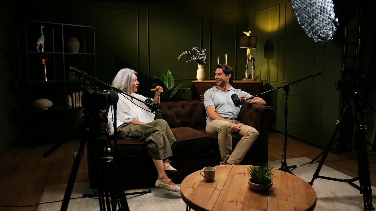 Two adults sitting on a sofa, discussing into microphones in a professional studio