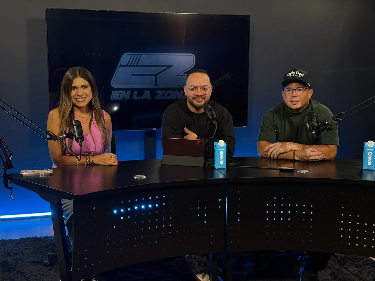 Three people sitting at a panel table during a broadcast or podcast recording with blue lighting and studio equipment