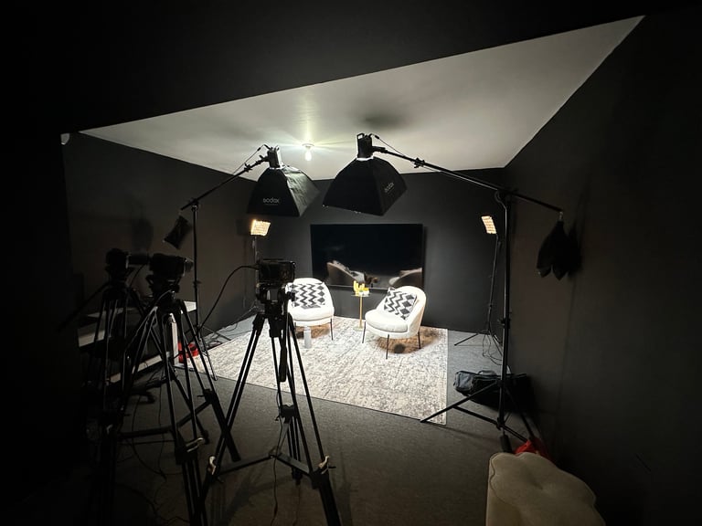 Professional film or photography studio set with mounted lights, tripods, chairs, and white backdrop under bright lighting